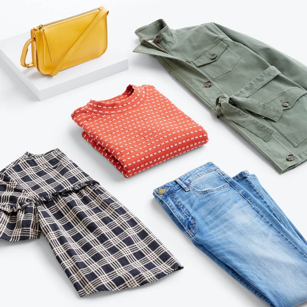 Stitch Fix women’s apple-picking outfit with authentic wash jeans, plaid blouse with ruffle detail, red and white intarsia mock turtleneck sweater, olive cargo jacket and yellow crossbody bag on platform.