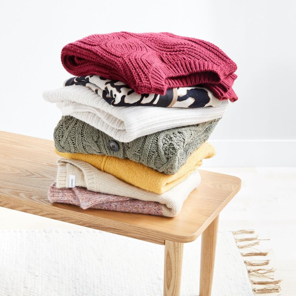 Stitch Fix women’s stacked folded sweaters in various colors and patterns on a bench.