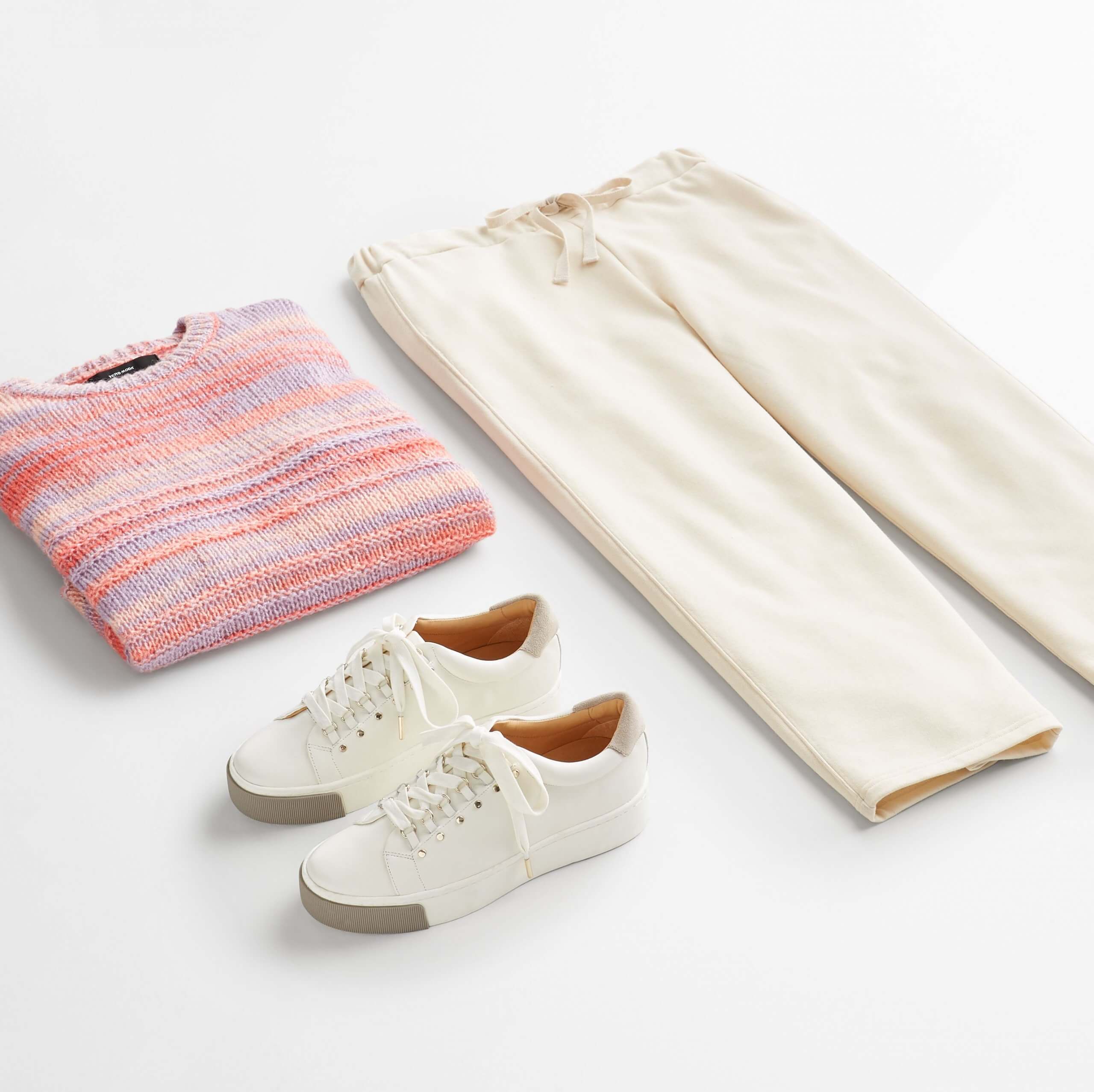 Stitch Fix women’s outfit laydown featuring gold accented white sneakers, pink and blue striped sweater and beige wide-leg pants.