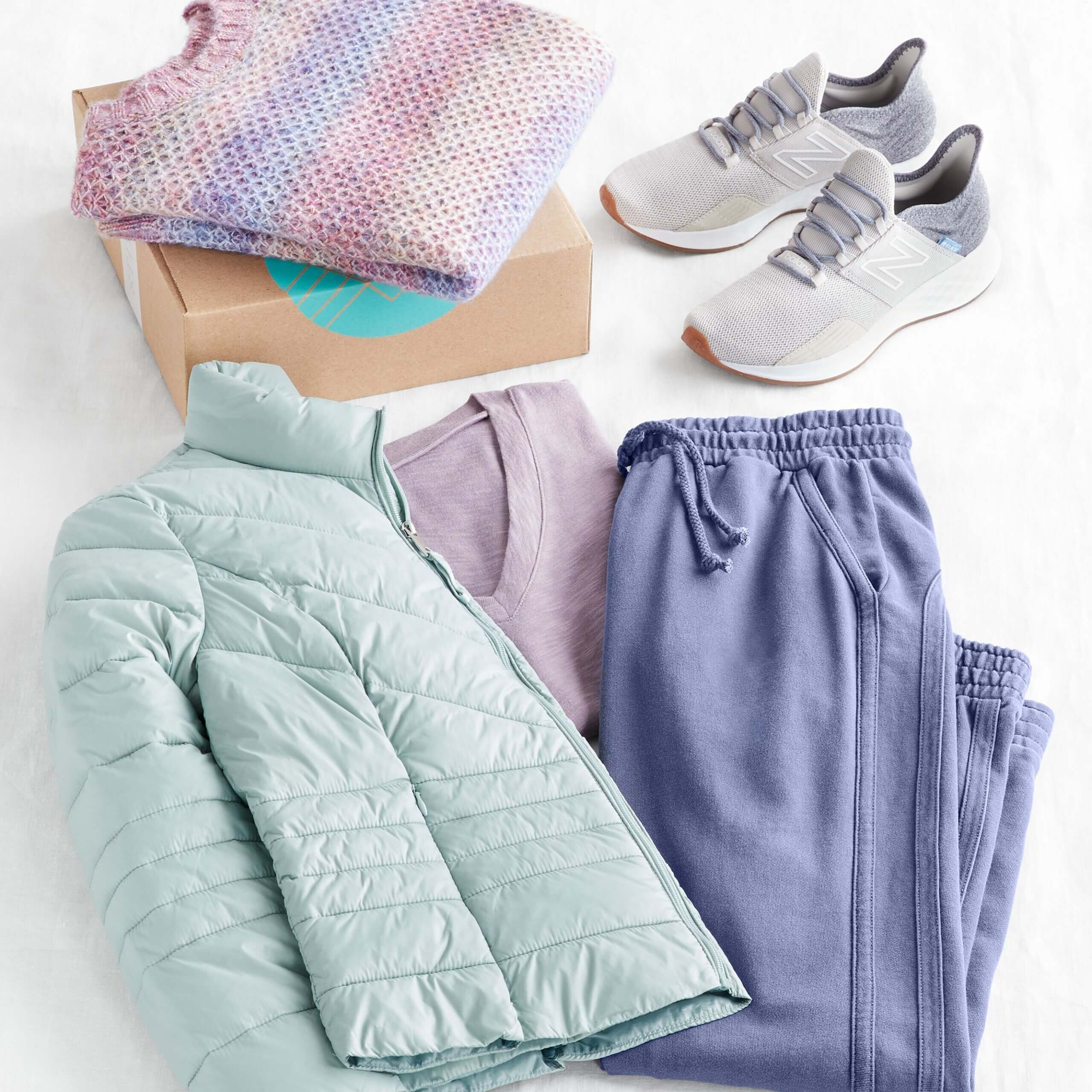 Stitch Fix Women's outfit laydown featuring mint puffer jacket, purple tee, blue jogger pants and grey sneakers, next to purple pullover on a Stitch Fix delivery box. 