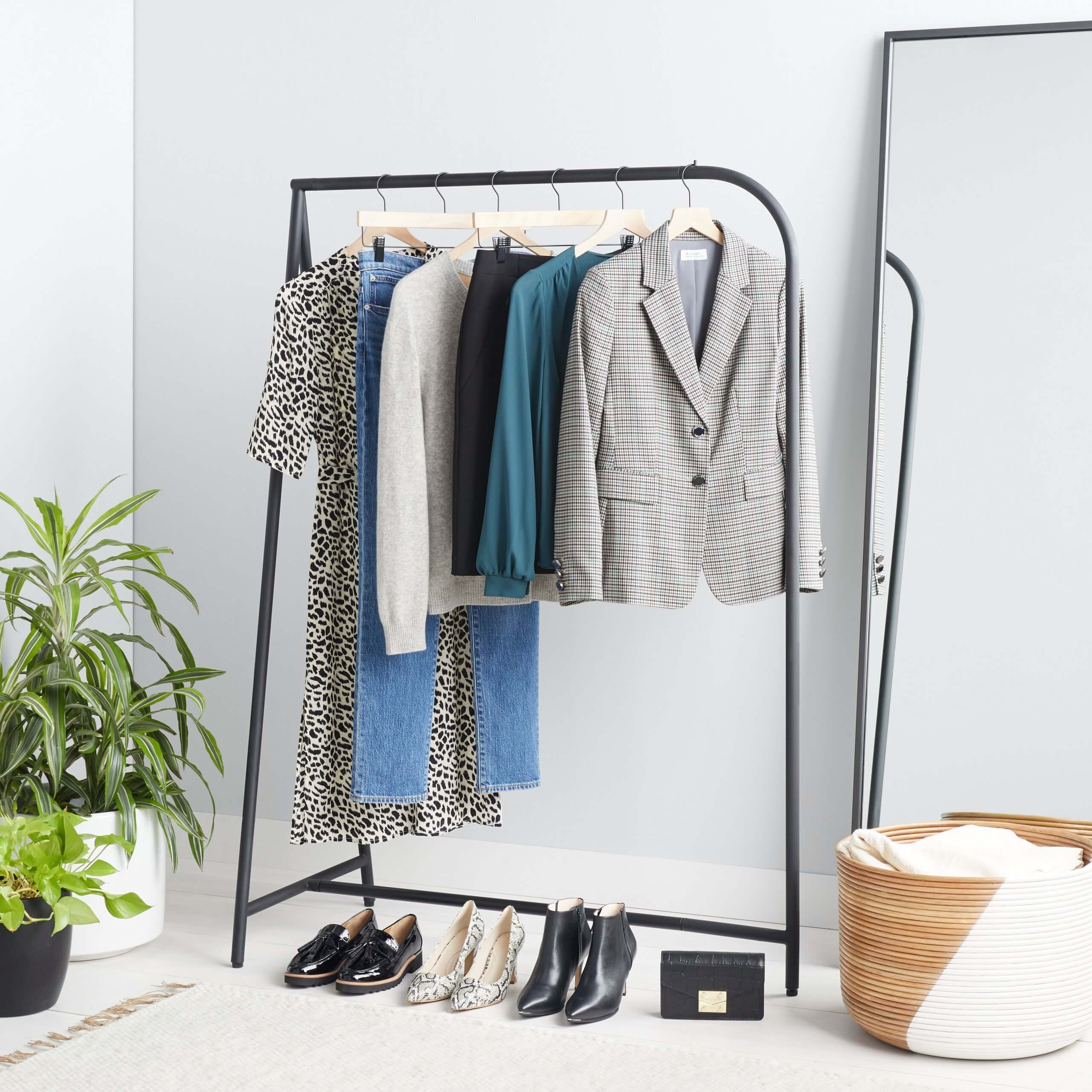 Stitch Fix Women’s rack image featuring grey blazer, teal blouse, black skirt, grey sweater, blue jeans and black animal print tie-waist dress hanging on black rack next to black purse, black booties, white animal print pumps and black loafers on the floor. 