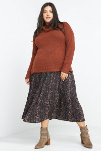 Stitch Fix model wearing plus-size clothing featuring orange cowl neck sweater, abstract printed midi skirt with taupe boots.