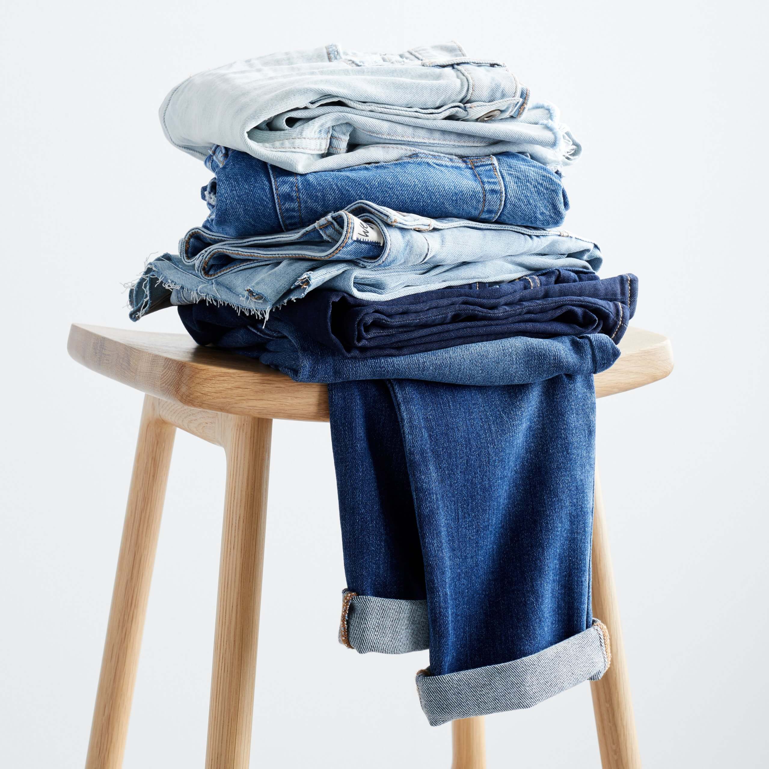 Stitch Fix women’s folded jeans in different washes on wooden stool.