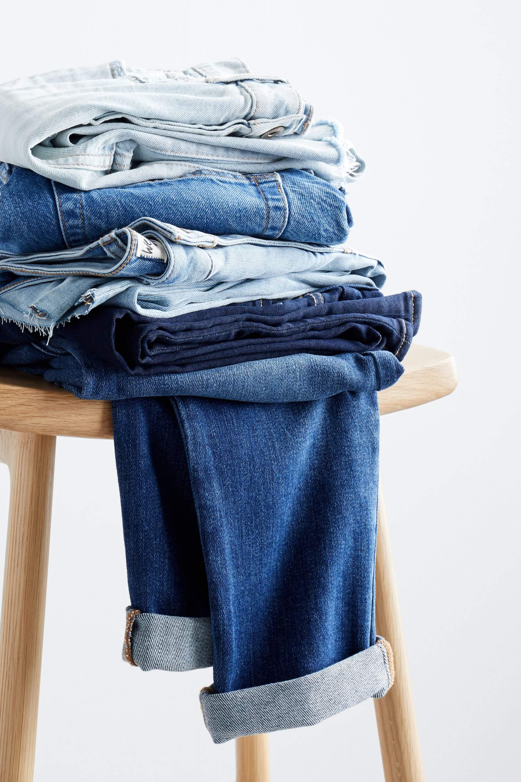 Stitch Fix women’s blue jeans in various washes folded and stacked on a wooden stool.
