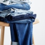 Stitch Fix jeans featuring five jeans in different blue washes stacked on a wood stool.