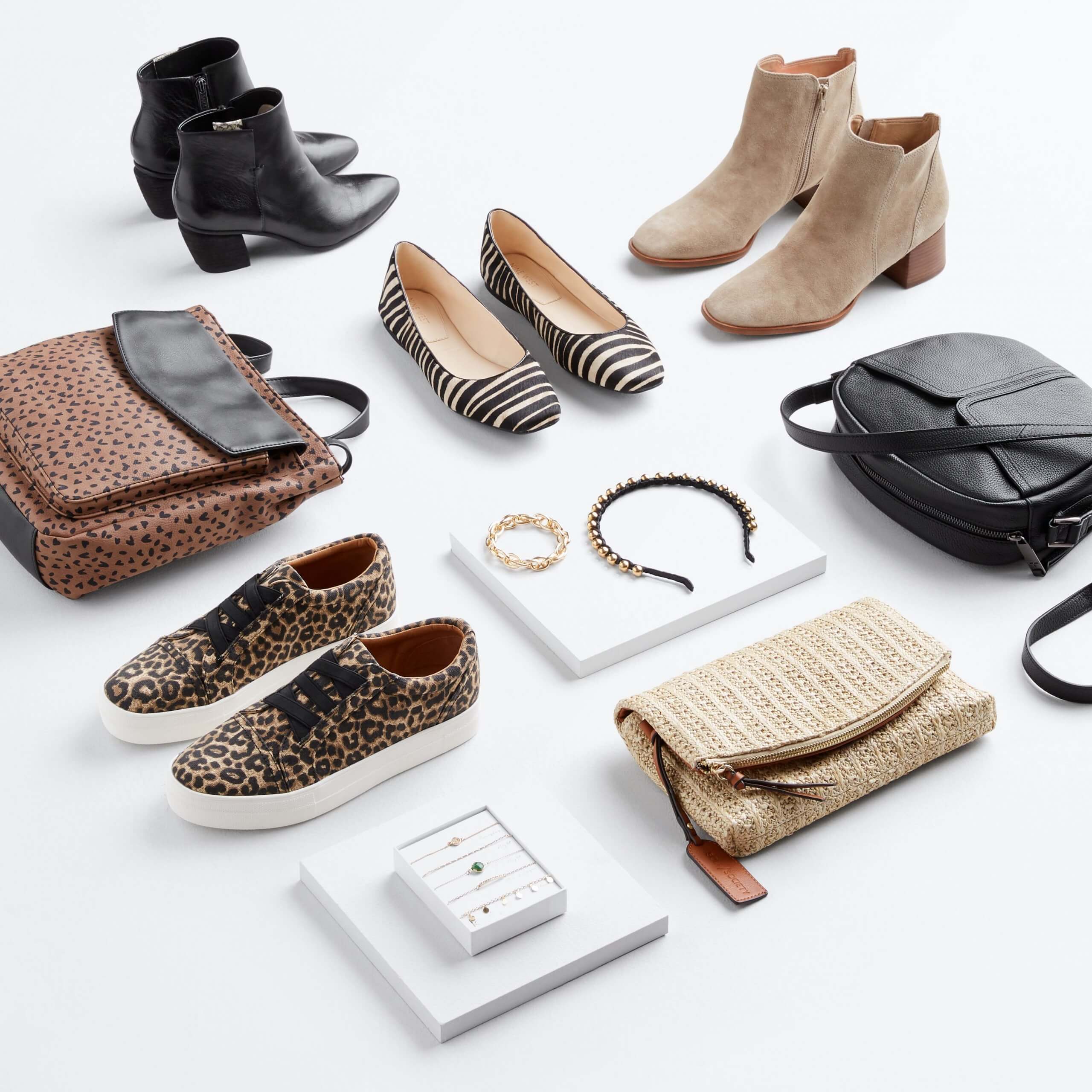 Stitch Fix Women’s laydown featuring black heeled booties, black striped flats, tan heeled booties, black purse, tan clutch, animal print sneakers and animal print purse on the floor with black headband and gold bracelets on white blocks. 