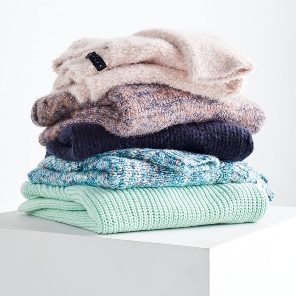 Stitch Fix women’s sweaters in mint green, blue speckled, navy, pink and purple speckled and blush stacked on a white pedestal.