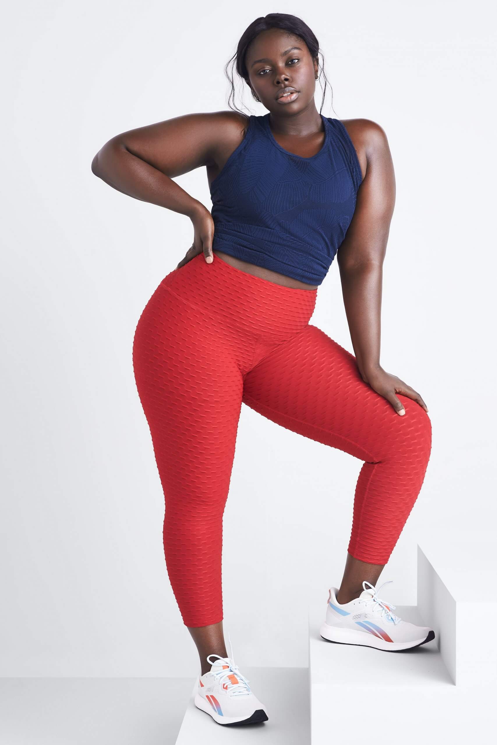 Stitch Fix women’s model wearing plus-size navy cropped tank, red textured leggings and red and blue accented white sneakers.