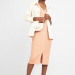 Stitch Fix women’s model in chic style outfit featuring peach midi-dress, off-white collared jacket, off-white crossbody bag and white sandals.