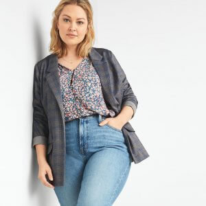 Stitch Fix model wearing women’s floral blouse with plaid blazer and light wash denim leaning against a wall.