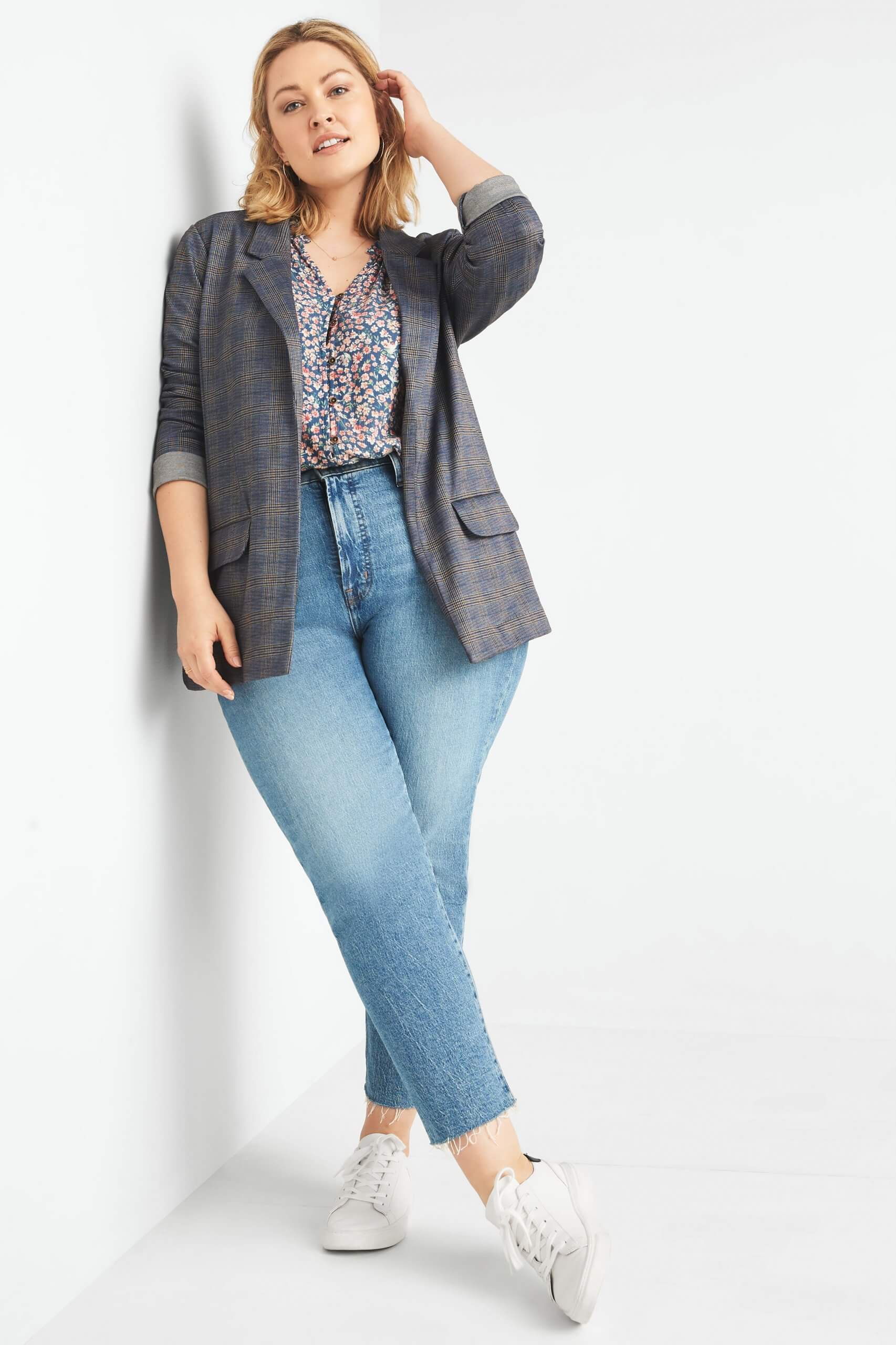Stitch Fix model wearing plus-size clothing featuring floral blouse, grey plaid blazer, light wash jeans and white sneakers.