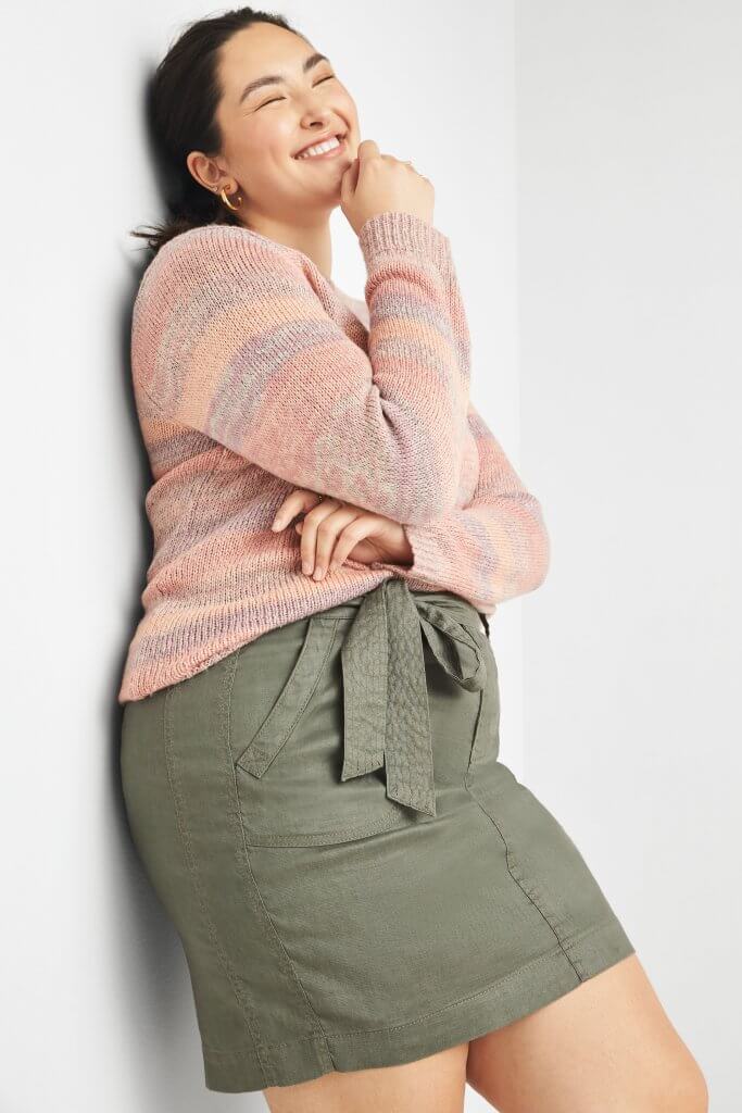 Stitch Fix model wearing gold hoop earrings, red, burgundy, and orange-striped sweater and tie-waist olive utility skirt.