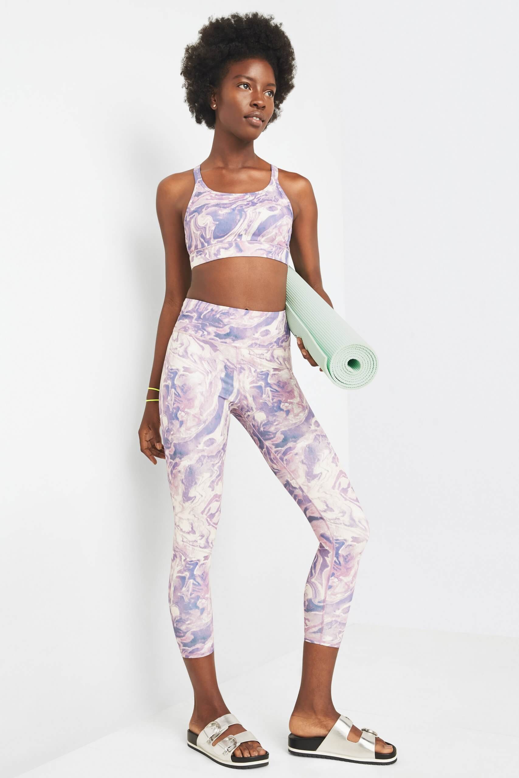 Stitch Fix model wearing eco-friendly workout clothing featuring matching purple calacatta print sports bra and leggings with a slide sandal.