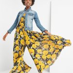 Stitch Fix women’s model wearing boho style yellow floral print jumpsuit with blue jean jacket and light blue chunky sandals.