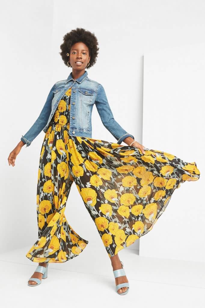 Stitch Fix women’s model wearing boho style yellow floral print jumpsuit with blue jean jacket and light blue chunky sandals.