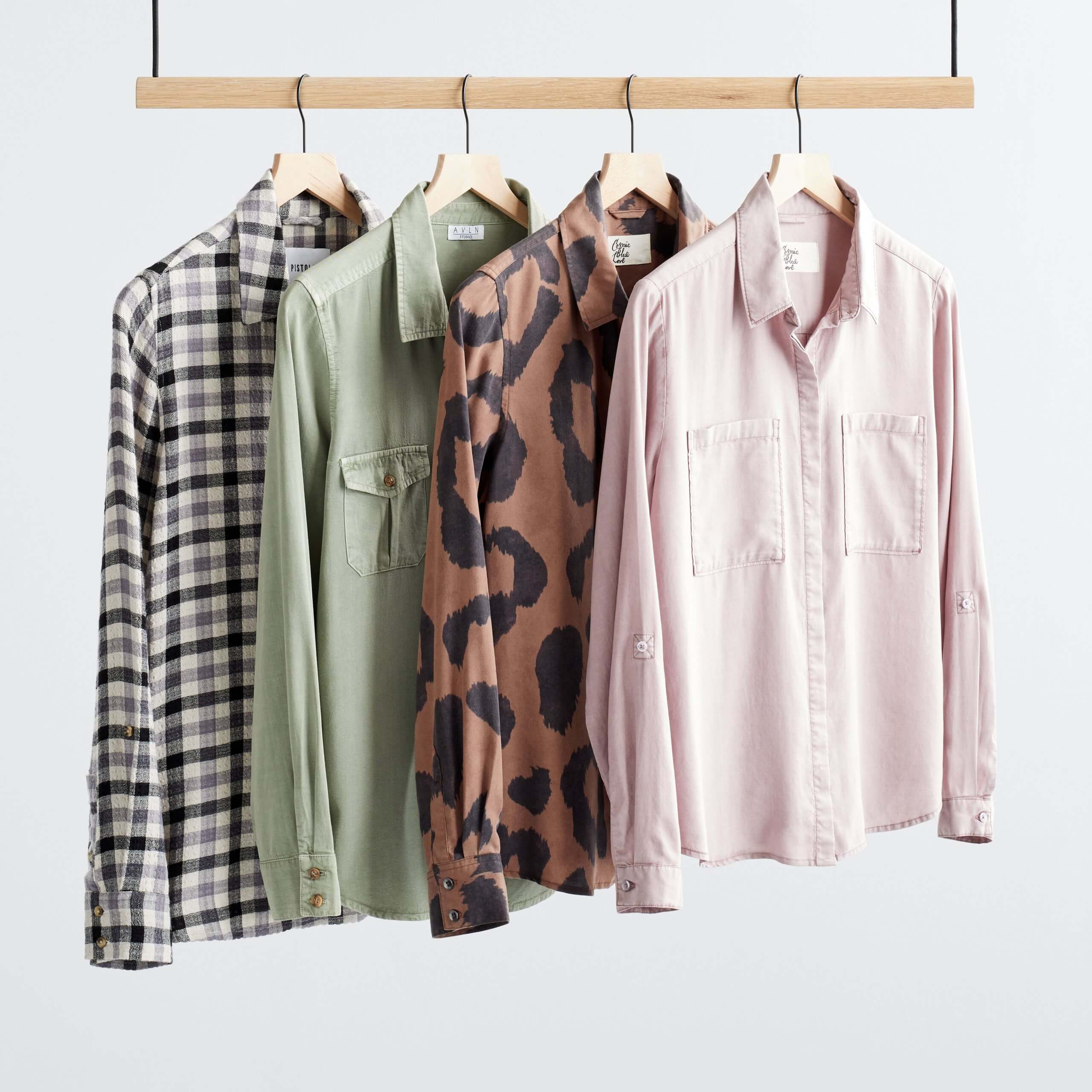 Stitch Fix Women’s rack featuring button-front shirts on wooden hangers in black and white plaid, olive green, brown leopard print and light pink.