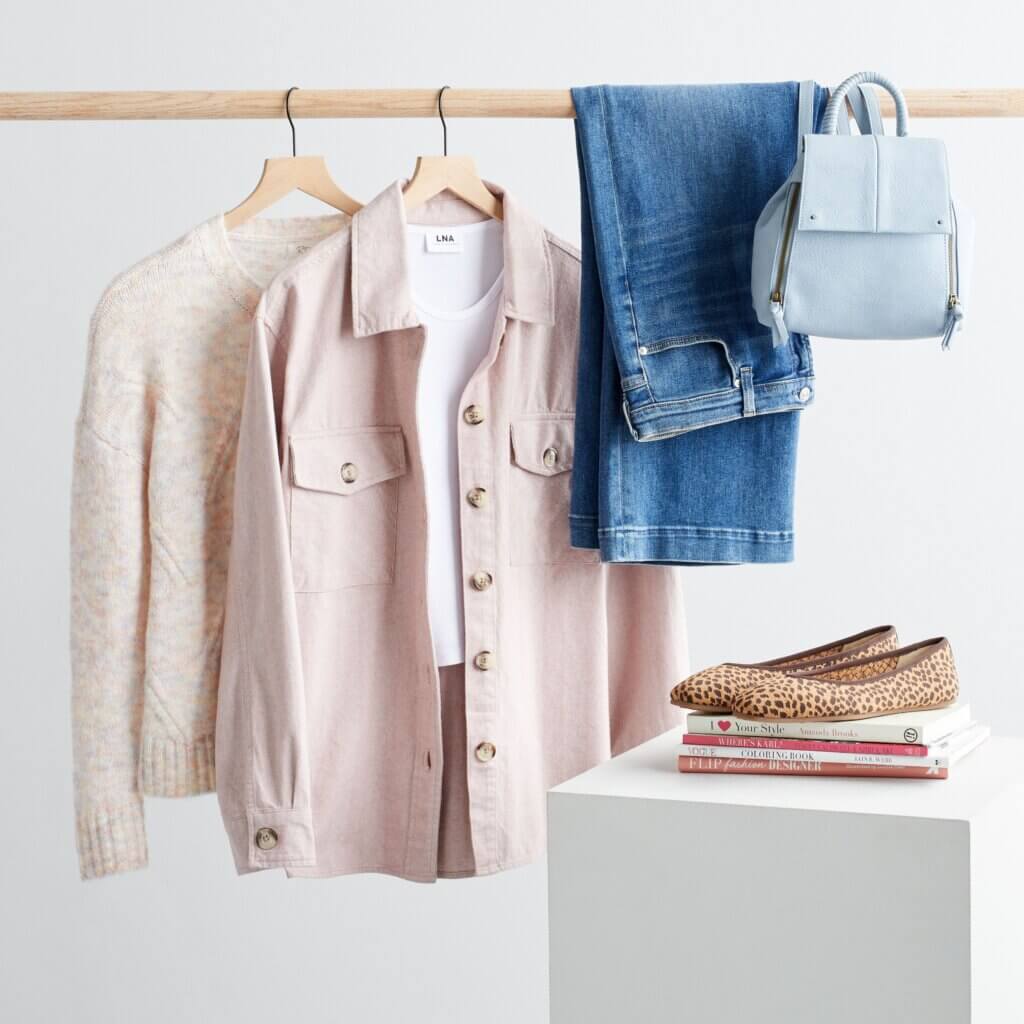 Stitch Fix women's petite with large bust outfit with jeans, backpack, shacket, top and sweater on rack and flats on books.