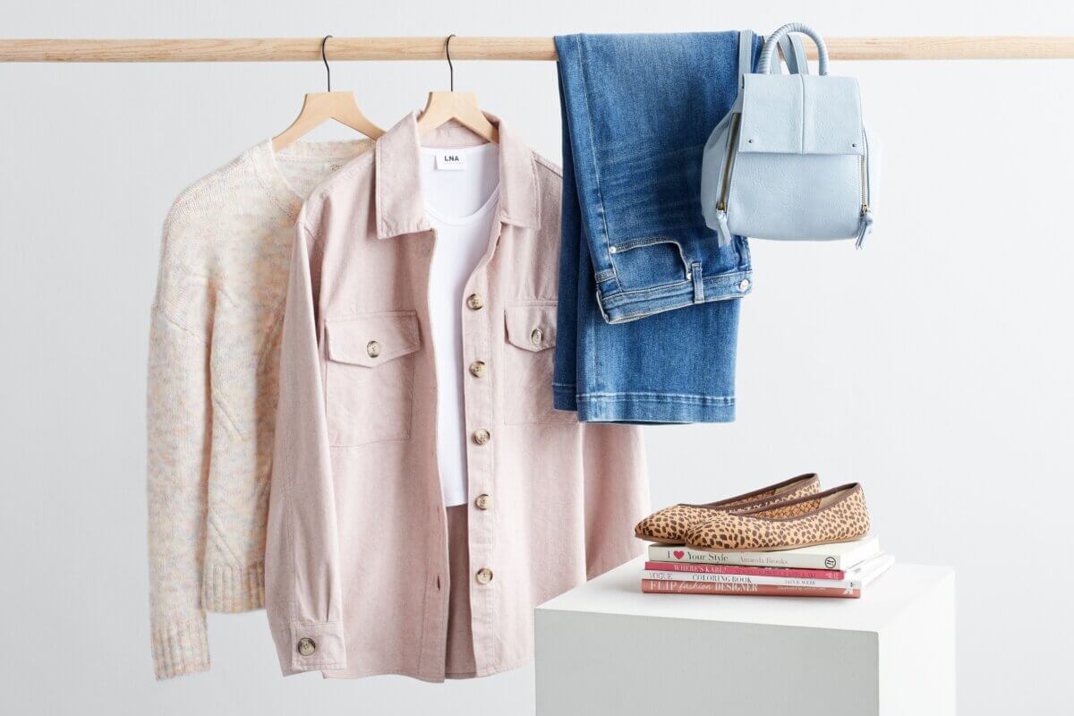 Stitch Fix women's shacket outfit featuring a white sweater, pink shacket over white T-shirt, blue jeans and light blue backpack on rack next to animal print flats on a stack of books.