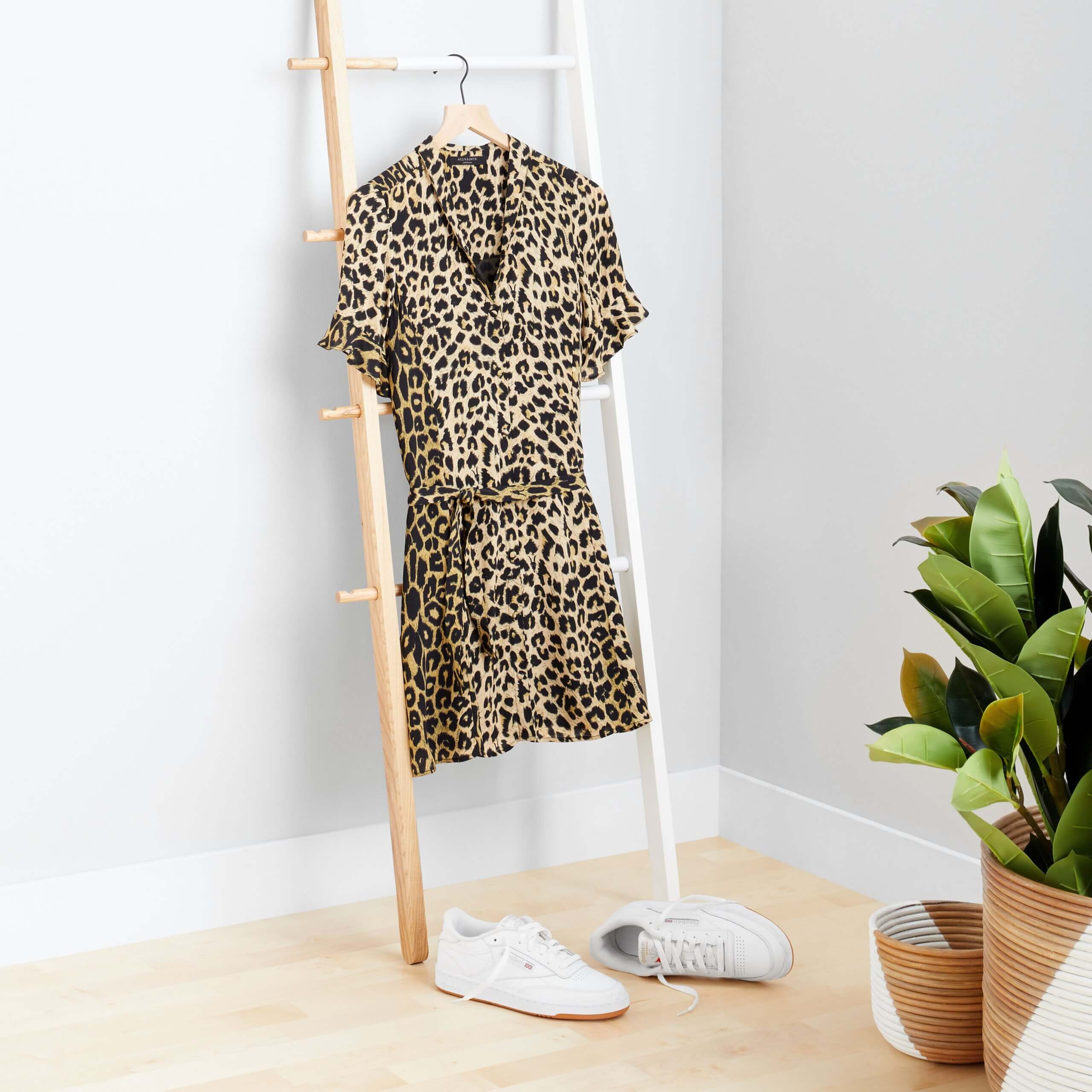Stitch Fix Women's rack image with brown cheetah print dress hanging on wooden rack with white sneakers on the floor. 