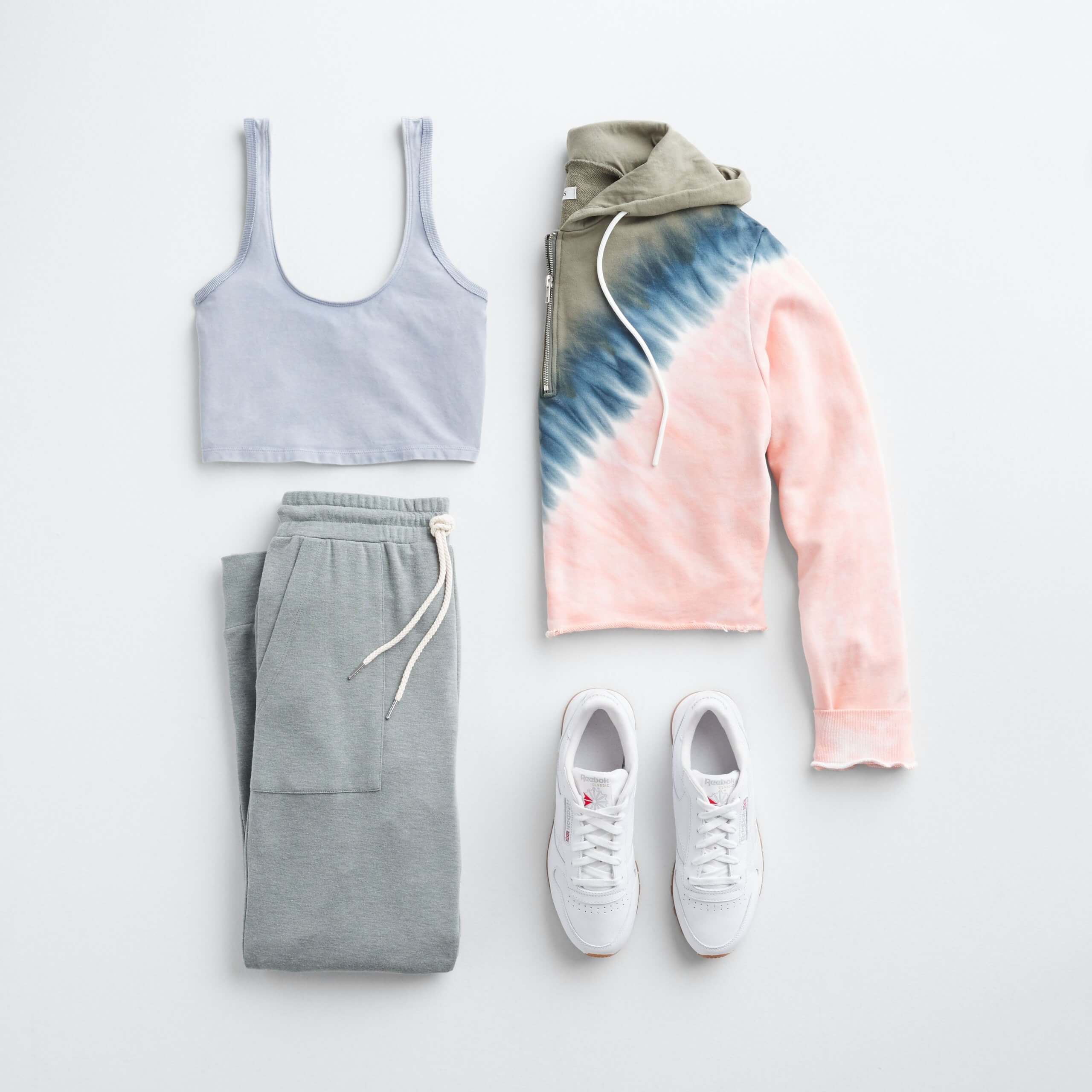 Stitch Fix women’s outfit laydown featuring white leather sneakers, light blue cropped tank, grey joggers and tie-dye hoodie.