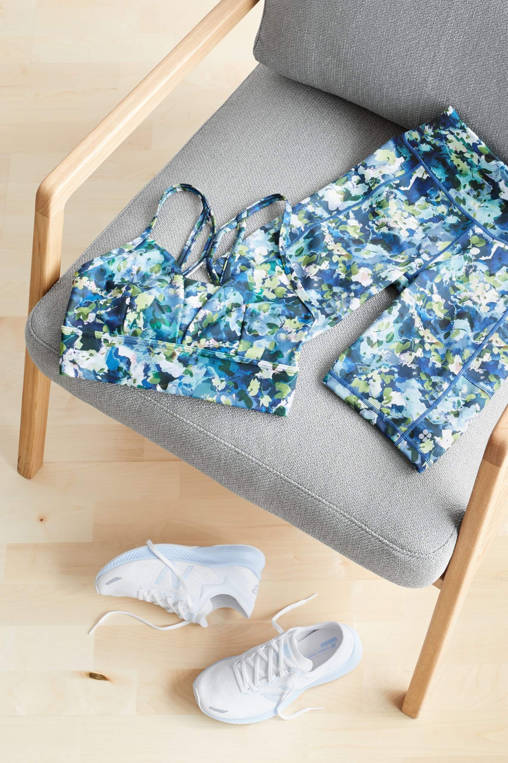 Stitch Fix women’s matching green and blue patterned sports bra and bike shorts laying on grey chair next to white sneakers.