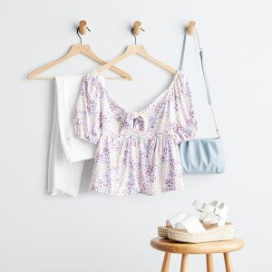 Stitch Fix women’s purple printed blouse with puff sleeves on hanger, white denim on hanger, blue purse on hanger and espadrille wedges on stool.