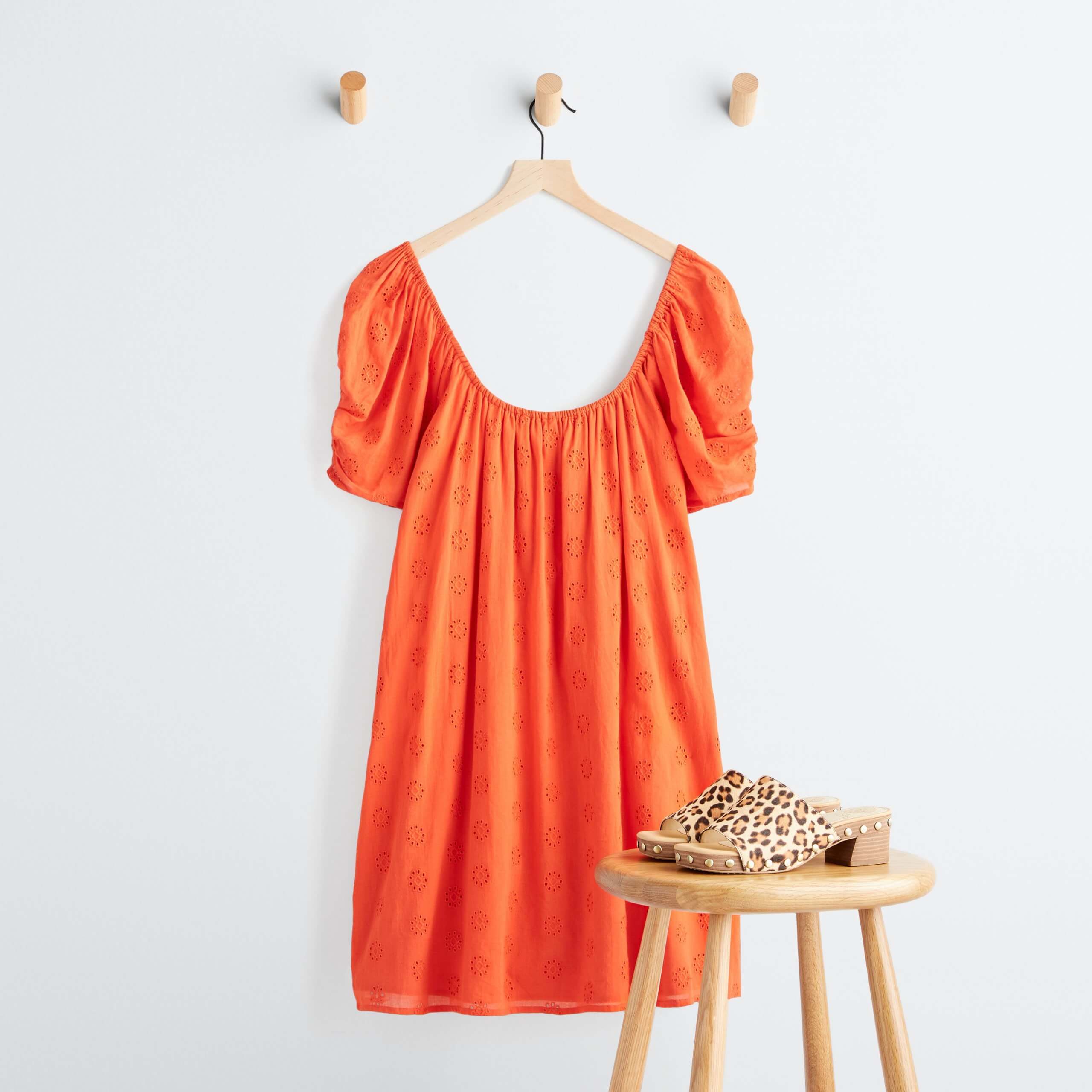 Stitch Fix Women’s orange textured dress hanging on a wooden hanger and leopard-print heeled mules on a wooden stool.