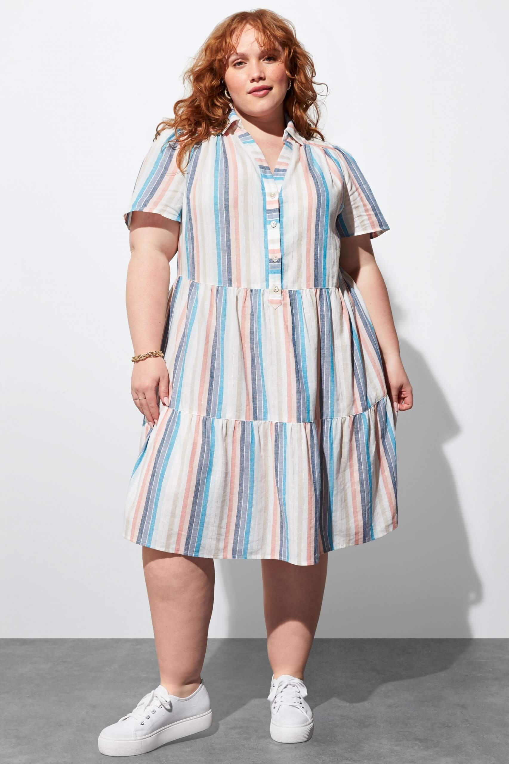 Stitch Fix Women's model wearing white, pink and blue striped shirt dress and white sneakers. 