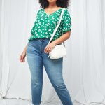 Stitch Fix model wearing plus-size women’s green floral blouse, blue denim capris, white sneakers and white crossbody bag.