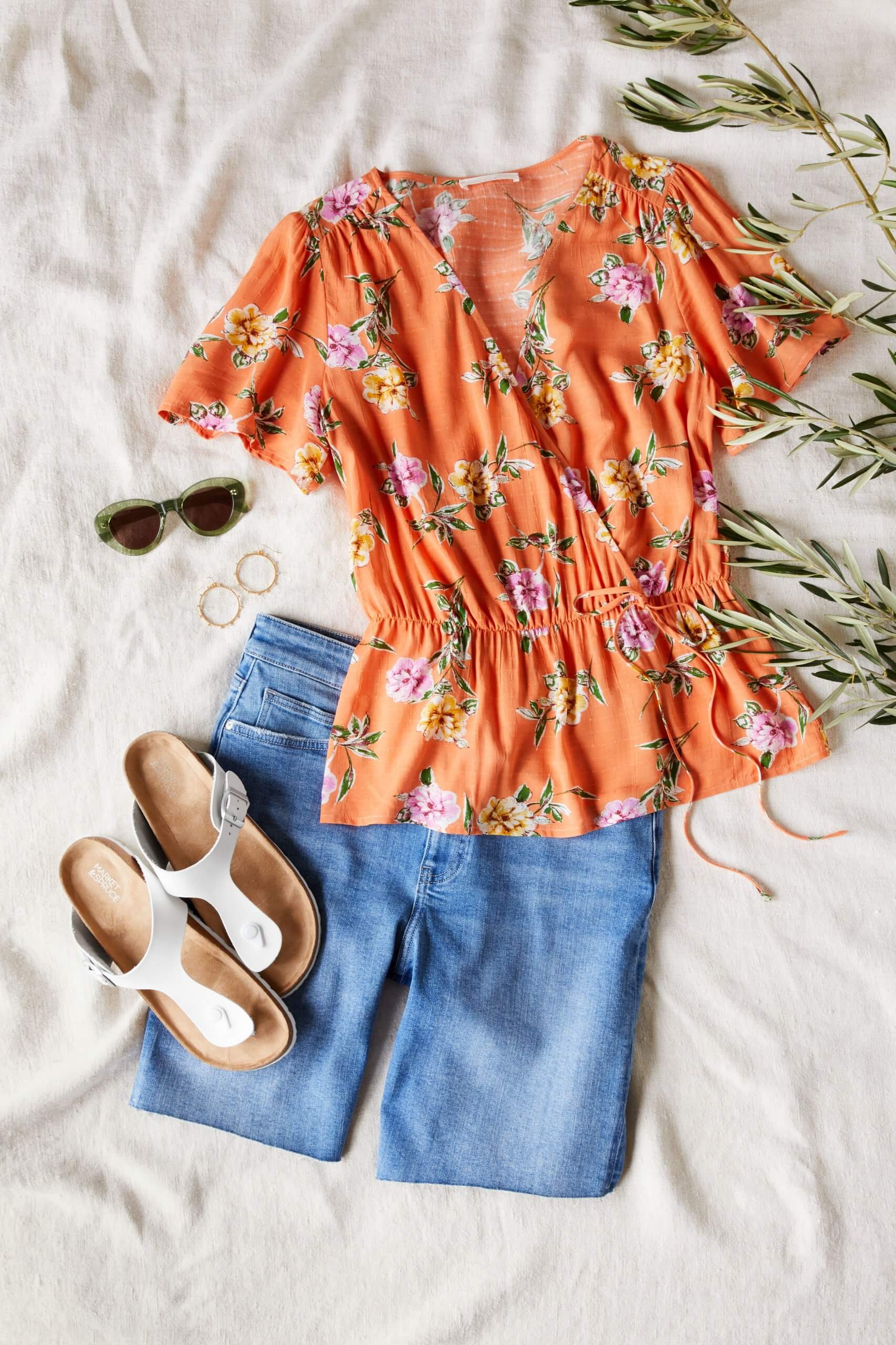 Stitch Fix Women's outfit laydown featuring orange floral wrap shirt, blue bermuda denim shorts, gold hoop earrings, white sandals and sunglasses. 