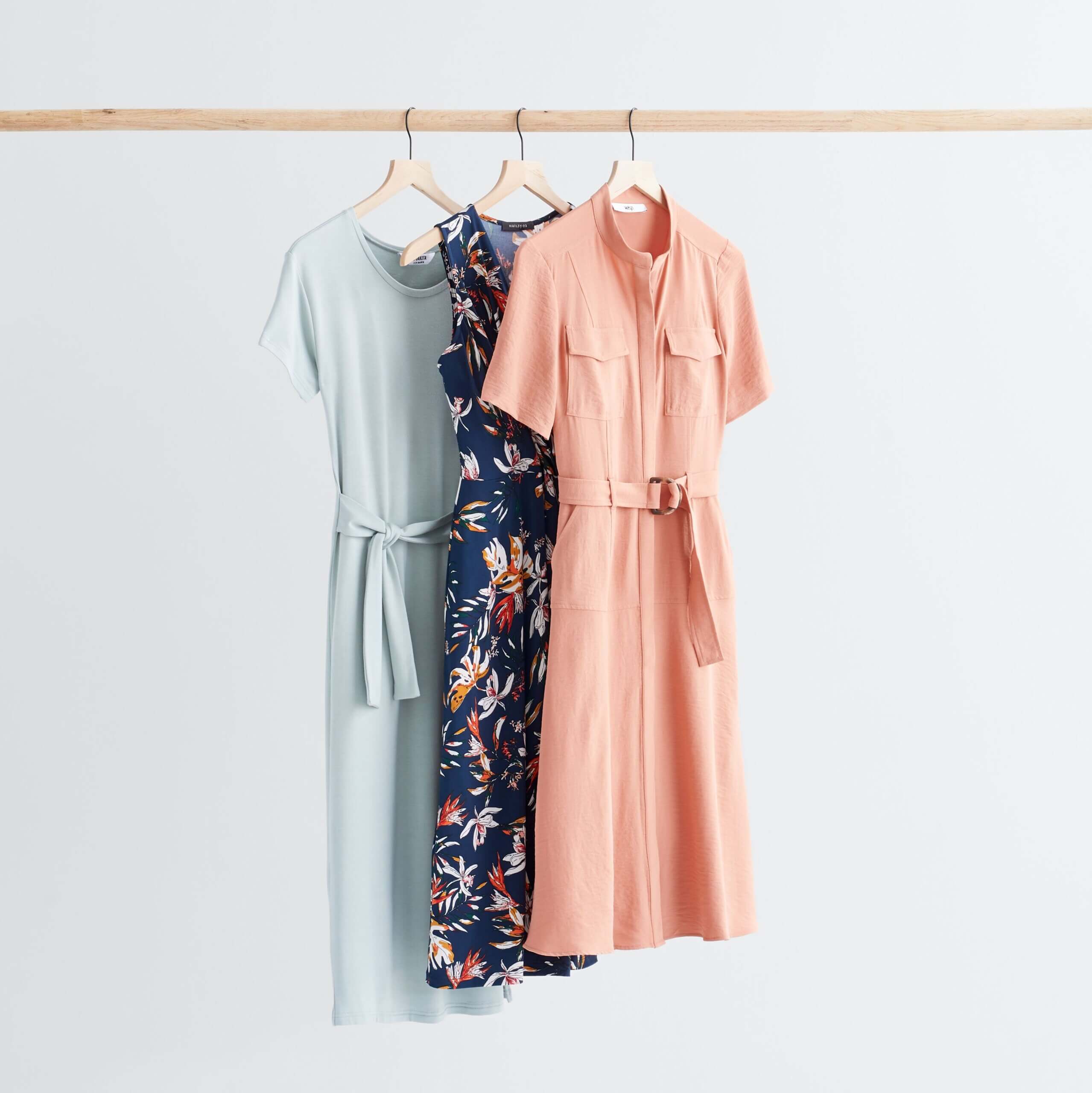 Stitch Fix Women’s rack image featuring pink shirt dress, navy floral dress and baby blue tie-waist dress hanging on wooden rack.
