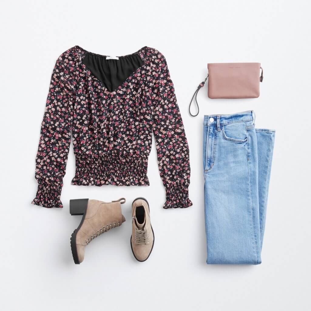 Stitch Fix women’s boots with jeans outfit featuring multi-colored smocked blouse, pink wristlet bag, light-wash jeans and tan ankle boots.