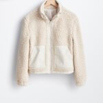 Stitch Fix model holding women’s off-white zip-up sherpa jacket on hanger.
