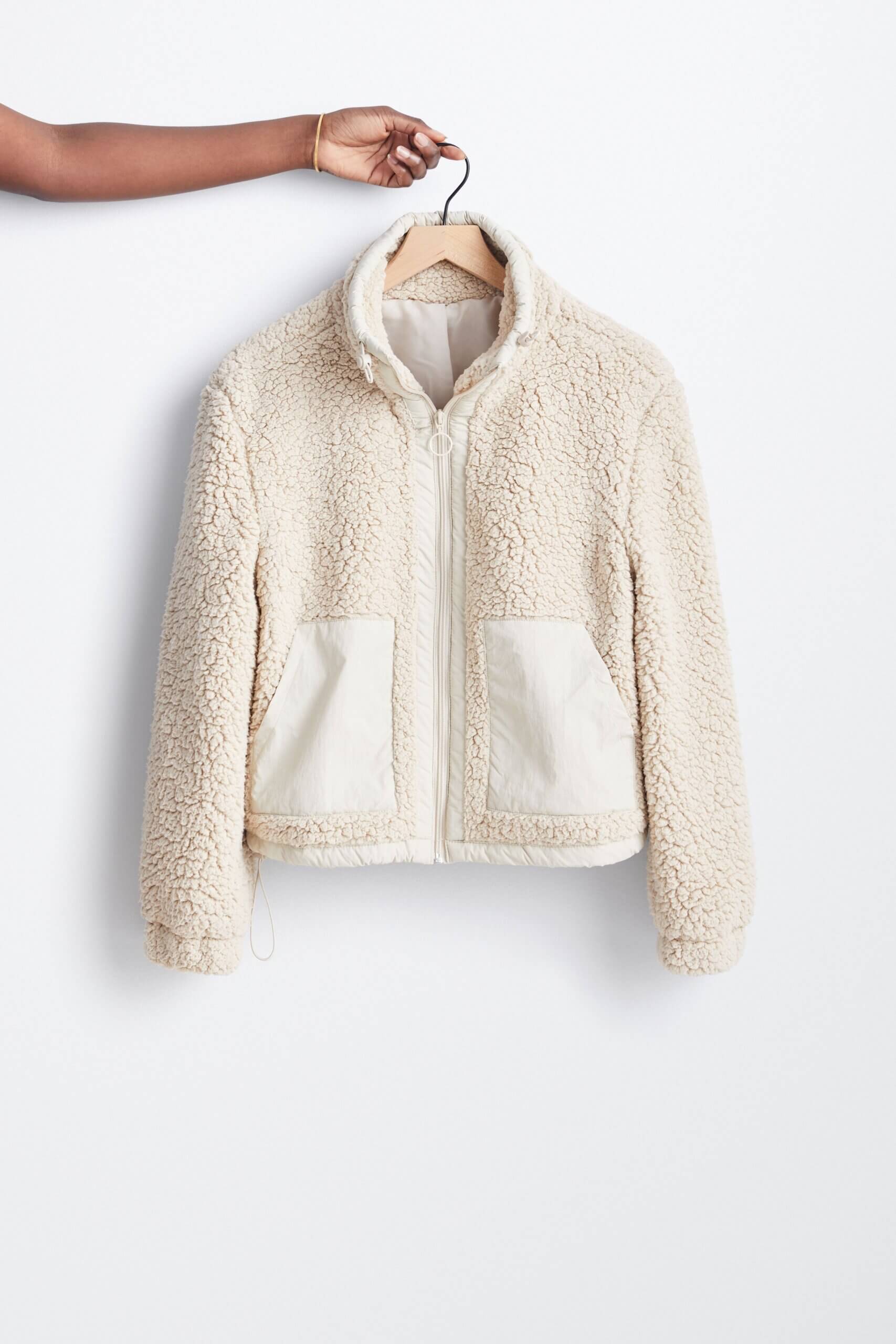Stitch Fix model holding women’s off-white zip-up sherpa jacket on hanger.
