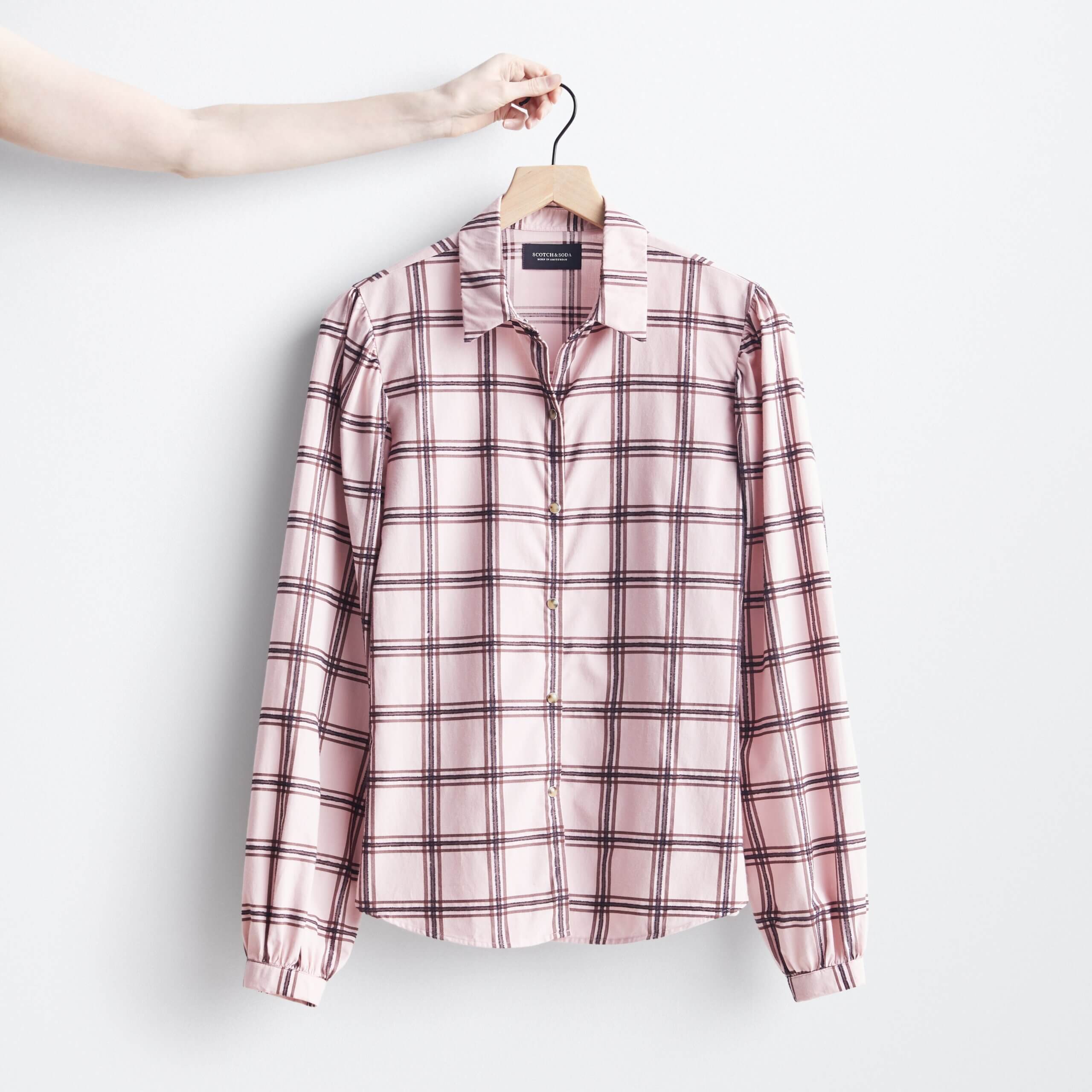 Stitch Fix women's pink and black plaid button-down shirt on hanger held by model.