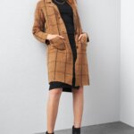 Stitch Fix women’s model in a dark academia aesthetic outfit featuring a black dress, tan windowpane-patterned cardigan and black booties.