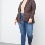 Stitch Fix women’s model wearing plus size business casual outfit with plaid blazer, beige turtleneck, blue skinny jeans, black loafers and gold accessories.