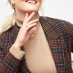 Stitch Fix women’s model wearing thick gold hoop earrings, tan turtleneck and plaid blazer.