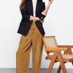Stitch Fix model in normcore aesthetic outfit for women featuring white crew neck sweater, black blazer, brown wide-leg trousers and black loafers.
