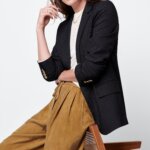 Stitch Fix women's normcore outfit on model wearing black blazer, white top and brown pleated pants.