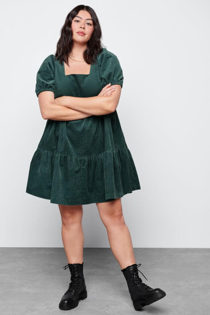 Stitch Fix women’s model in dark academia aesthetic outfit featuring a hunter green babydoll dress and black lace-up combat boots.