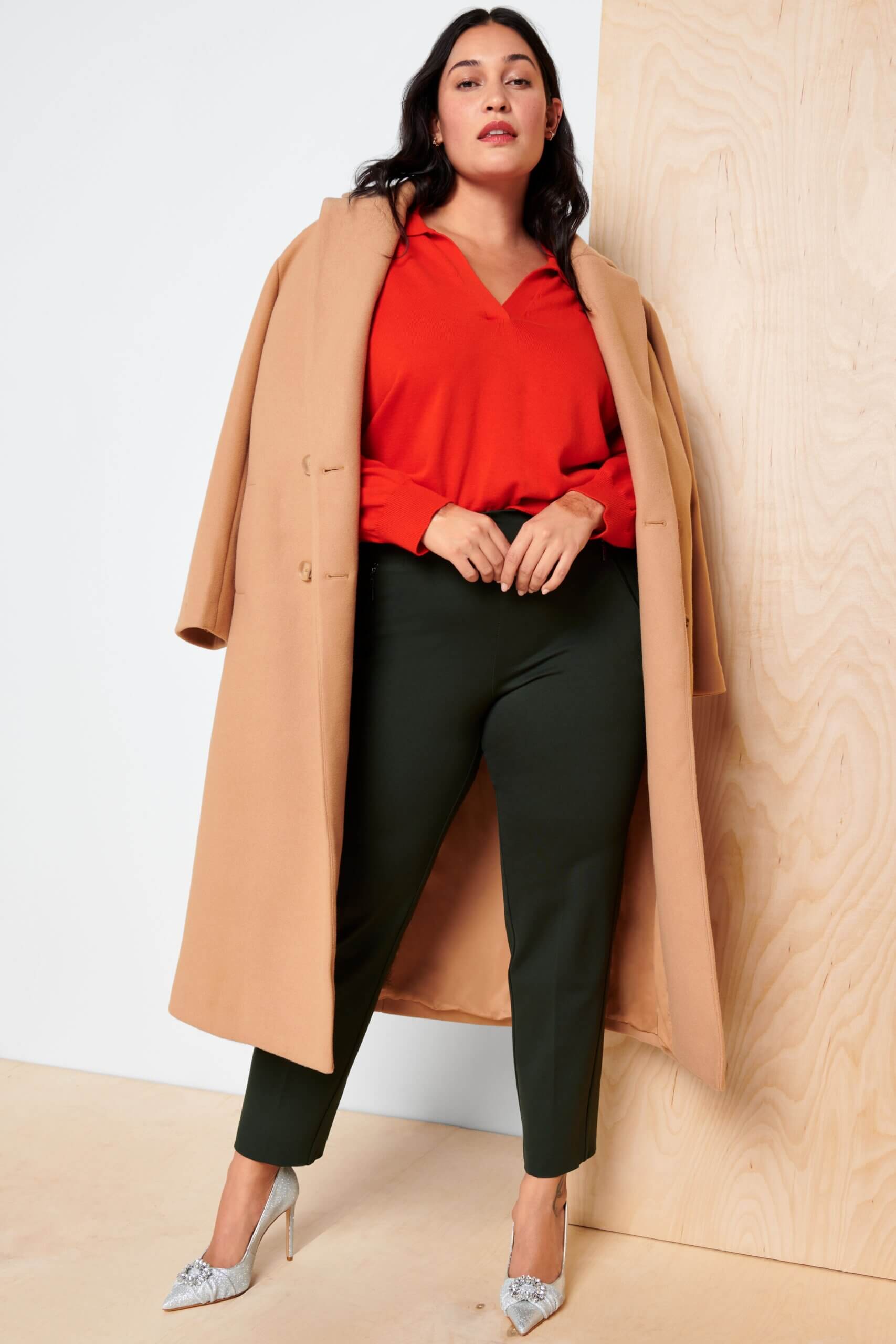 Stitch Fix model wearing women’s brown, red and black outfit with red blouse, camel coat, black pants and silver heels.
