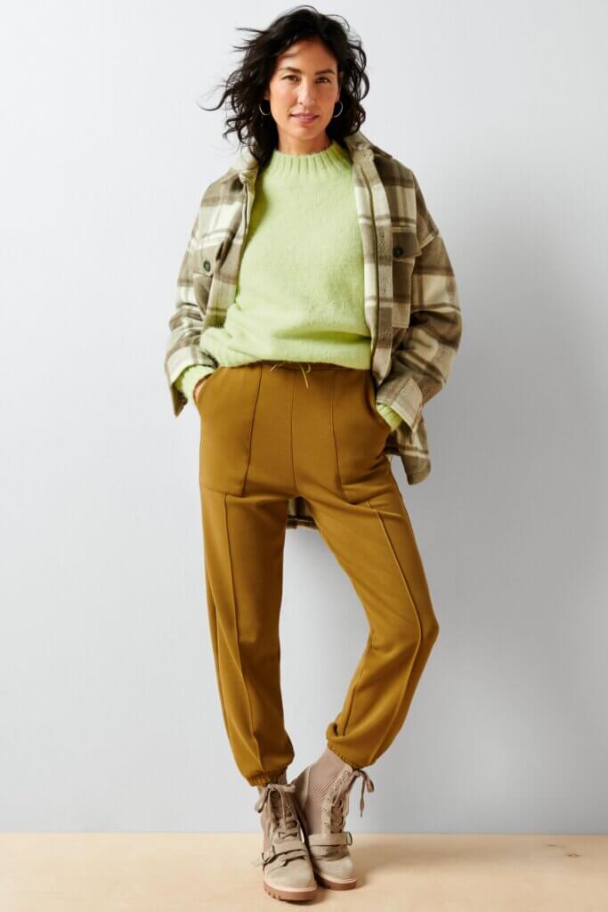 Stitch Fix women’s model wearing olive sweatpant, lime green sweater, plaid shacket, and tan suede lug boots.