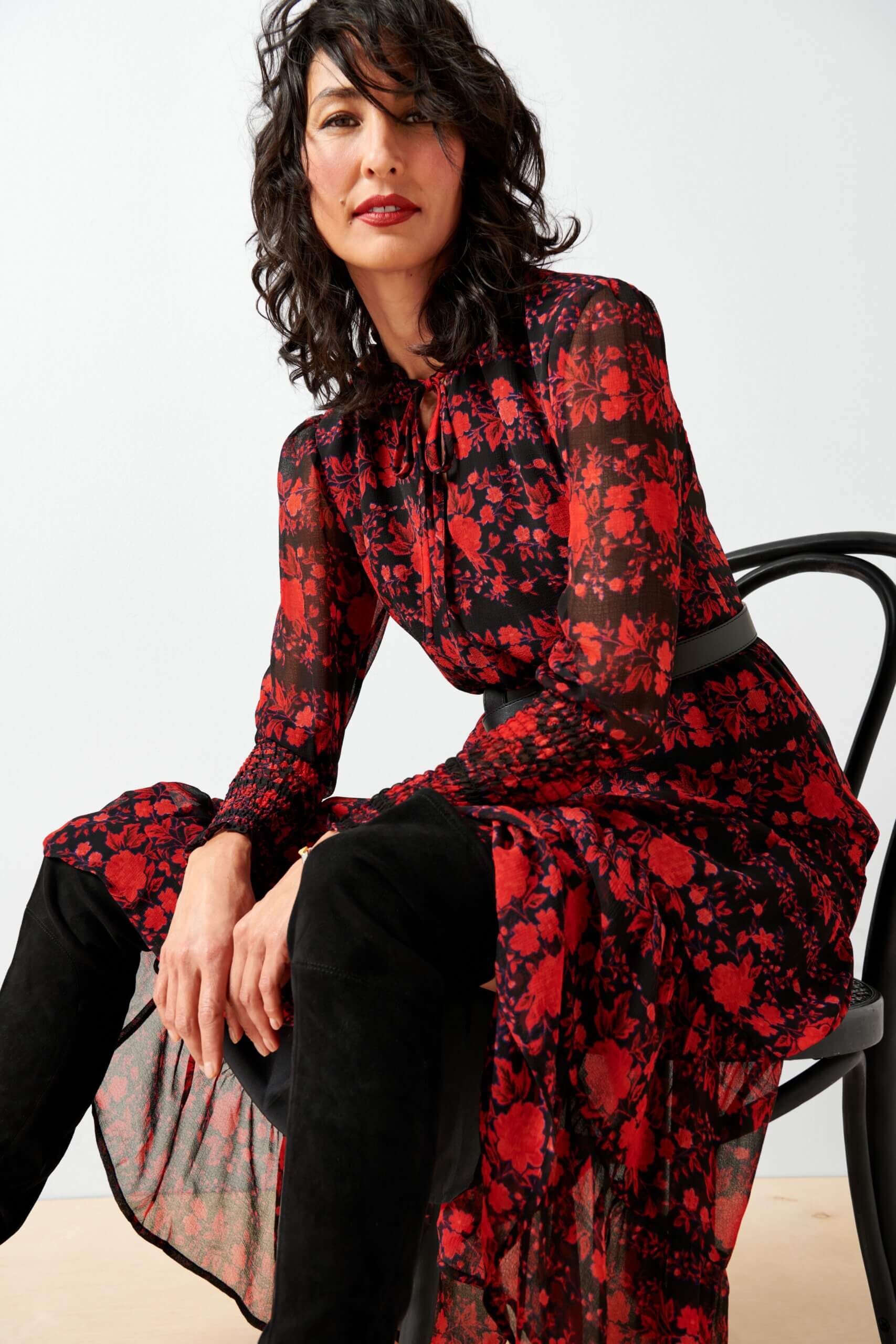 Stitch Fix model wearing women’s black and red outfit sitting on chair with floral dress and black over-the-knee suede boots.
