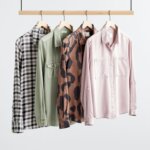 Stitch Fix Women’s blue plaid, solid green, abstract animal print and sold pink button-ups handing on a rack.
