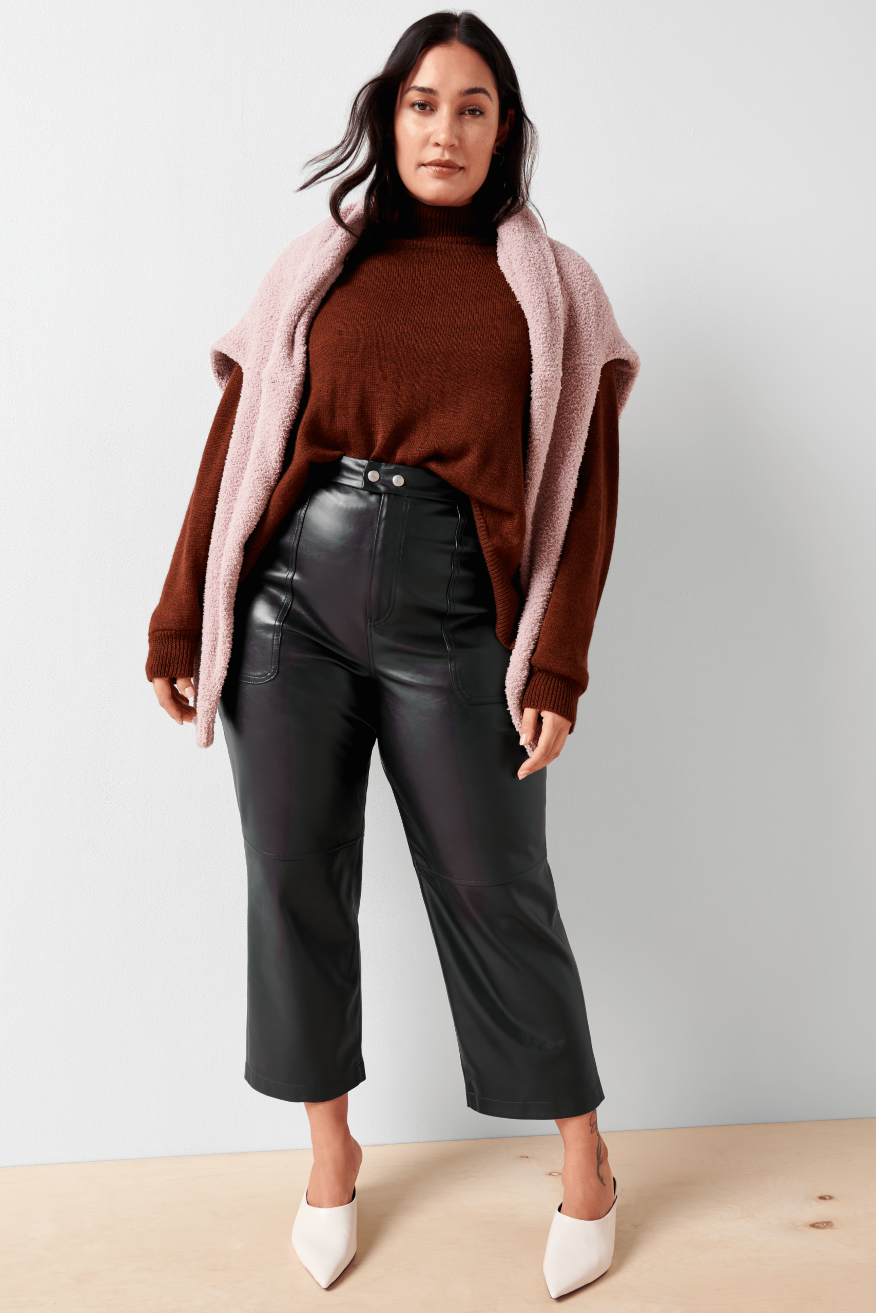 Stich Fix Women’s model wearing a cozy fall aesthetic outfit with leather pants, burgundy turtleneck, pink sweater and white mules.