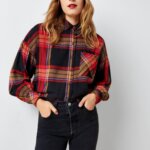 Stitch Fix Women’s model wearing a grunge outfit with black jeans, red and black plaid shirt and red beanie.