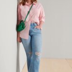 Stitch Fix Women’s model wearing a pink button-up, blue distressed jeans, white sneakers, green crossbody bag and white cap.