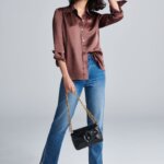 Stitch Fix Women’s model wearing a brown satin button-up, blue jeans, silver booties and black shoulder bag.