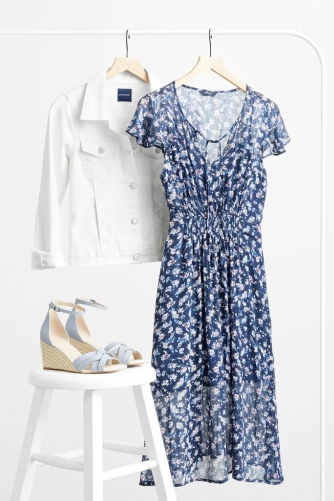 Stitch Fix women’s floral print accessorized navy blue dress for a wedding with pale blue wedges and white denim jacket.